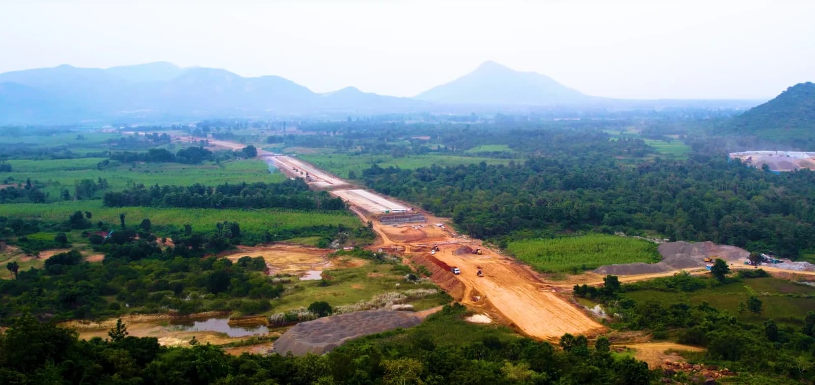 Aerial view of an under construction national highway in India surrounded by green landscape.