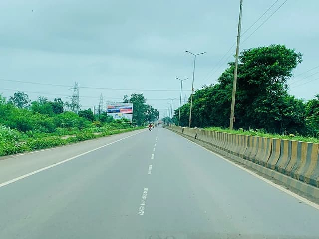 An empty highway in Chhattisgarh, India, flanked by trees and power lines.