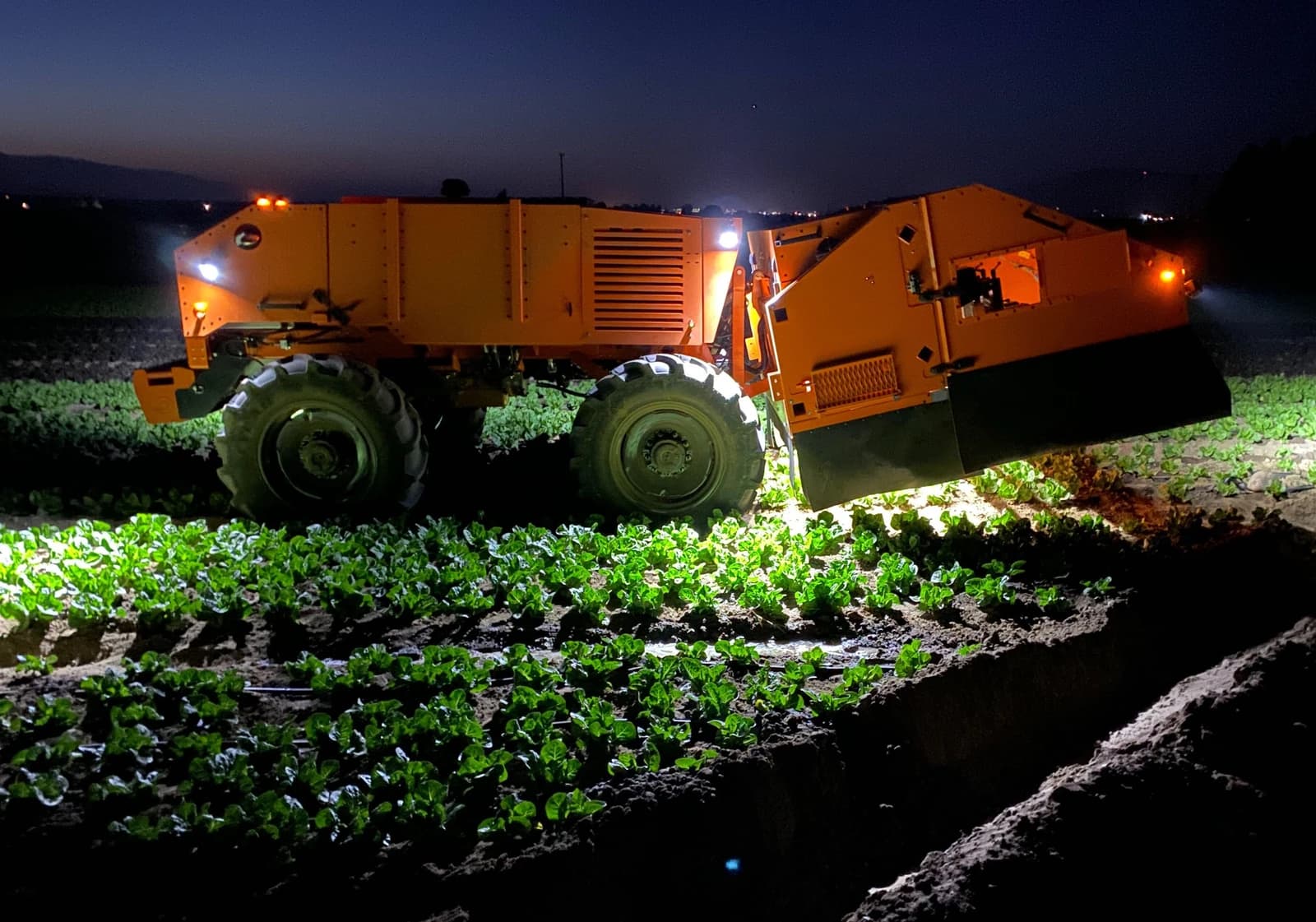 An orange robotic precision weeder, named Titan FT35, operates in a field at night.