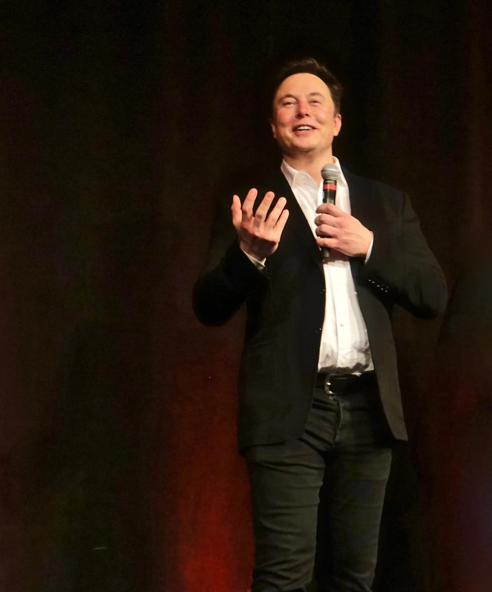 Elon Musk, CEO of Tesla, speaking into a microphone on stage.