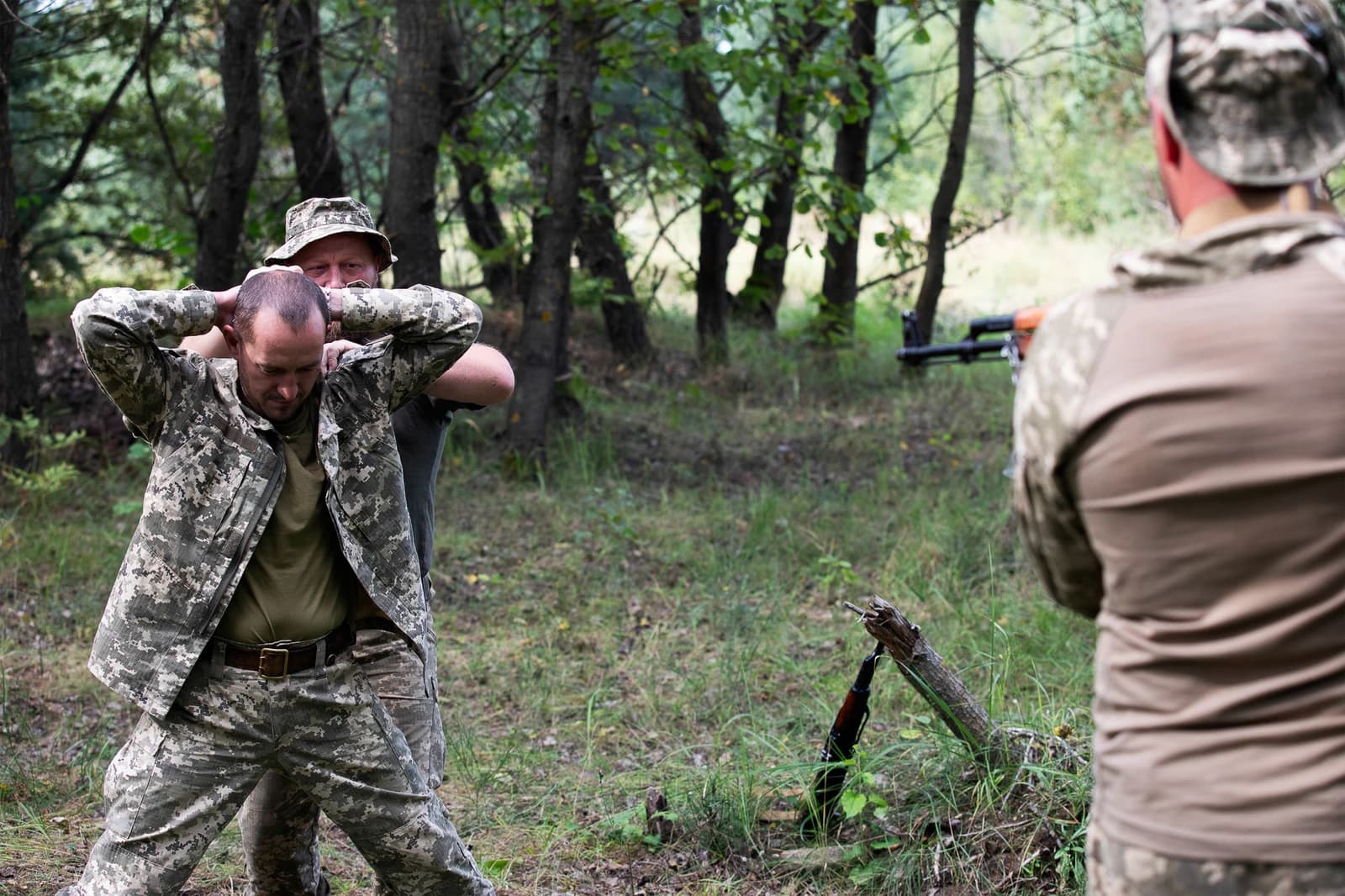 Ukrainian soldiers receiving field training from military advisors in a wooded area.