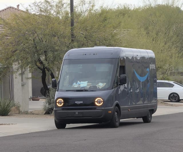 An Amazon electric delivery van with Prime logo driving on a residential street.