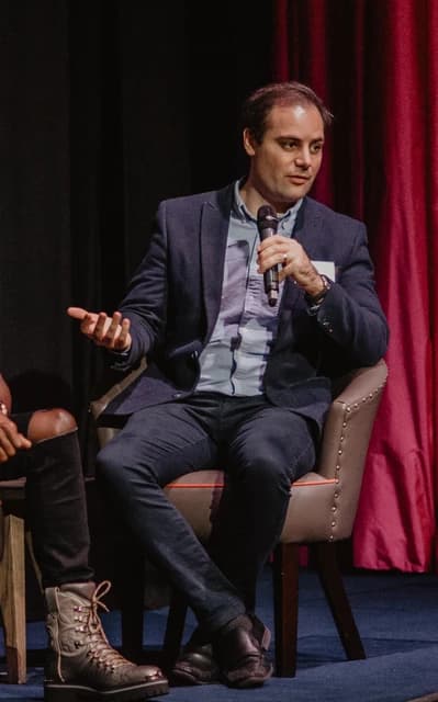 Ben Delo, BitMEX co-founder, speaking into a microphone at a conference.