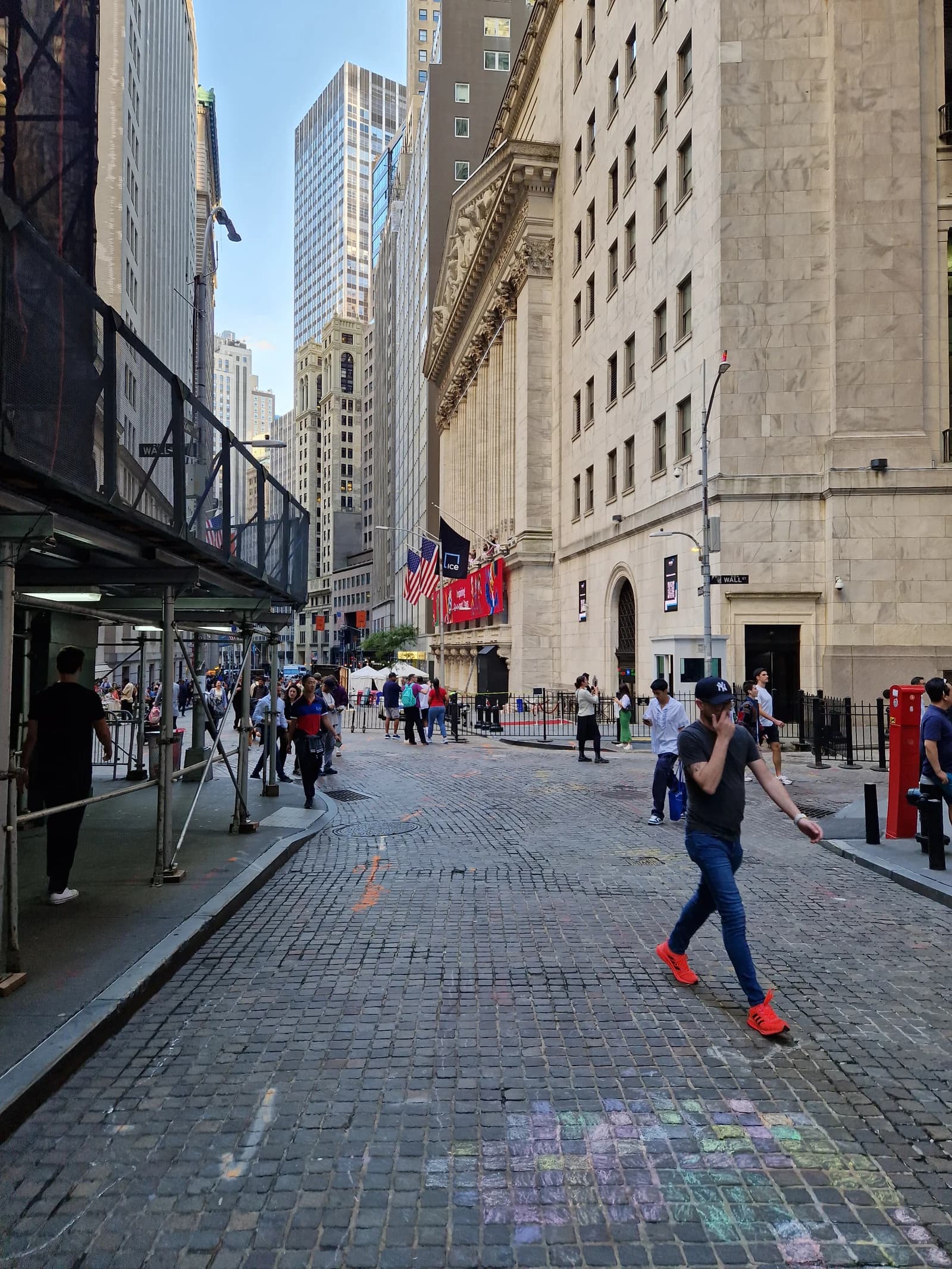 People walk on a cobblestone street in front of the New York Stock Exchange building.
