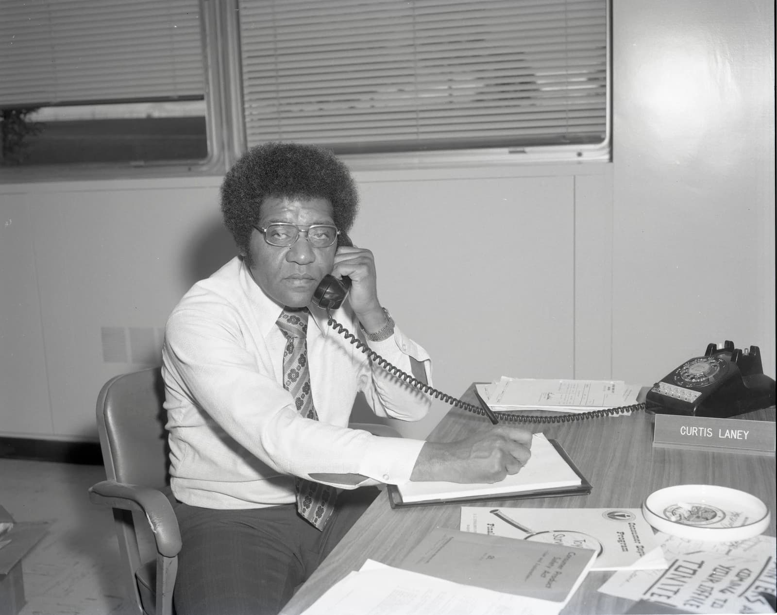 Curtis Laney, Consumer Protection Office employee, on a rotary phone at his desk.