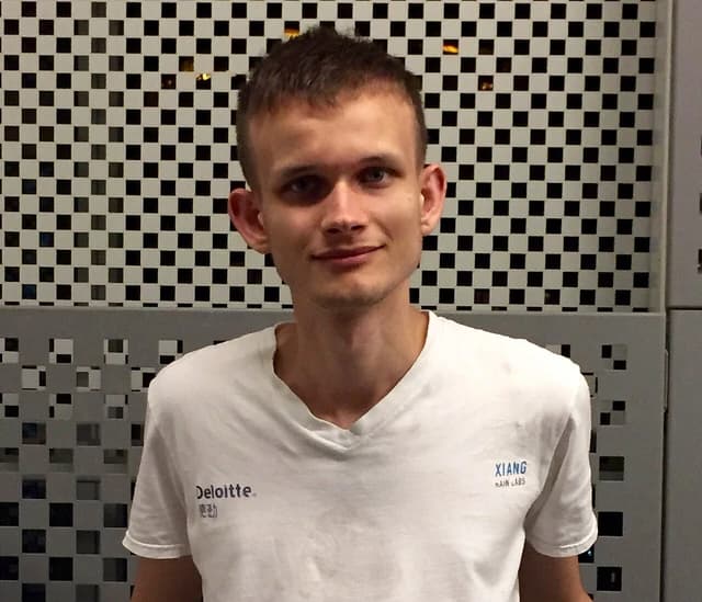 Vitalik Buterin, co-founder of Ethereum, stands smiling in front of a patterned wall.