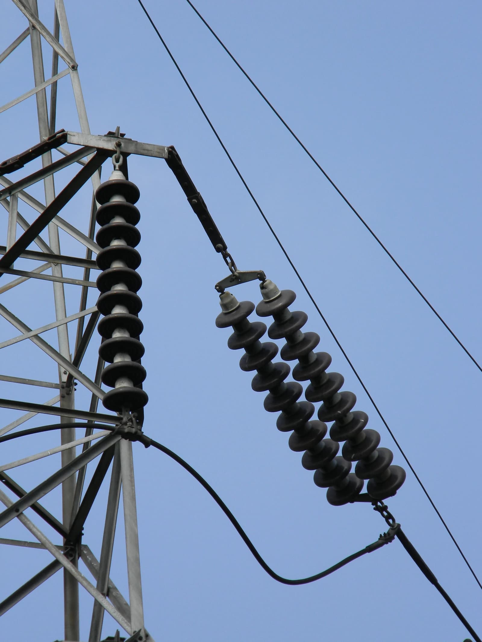 High voltage transmission line insulators connected to a metal tower, viewed against a clear blue sky.
