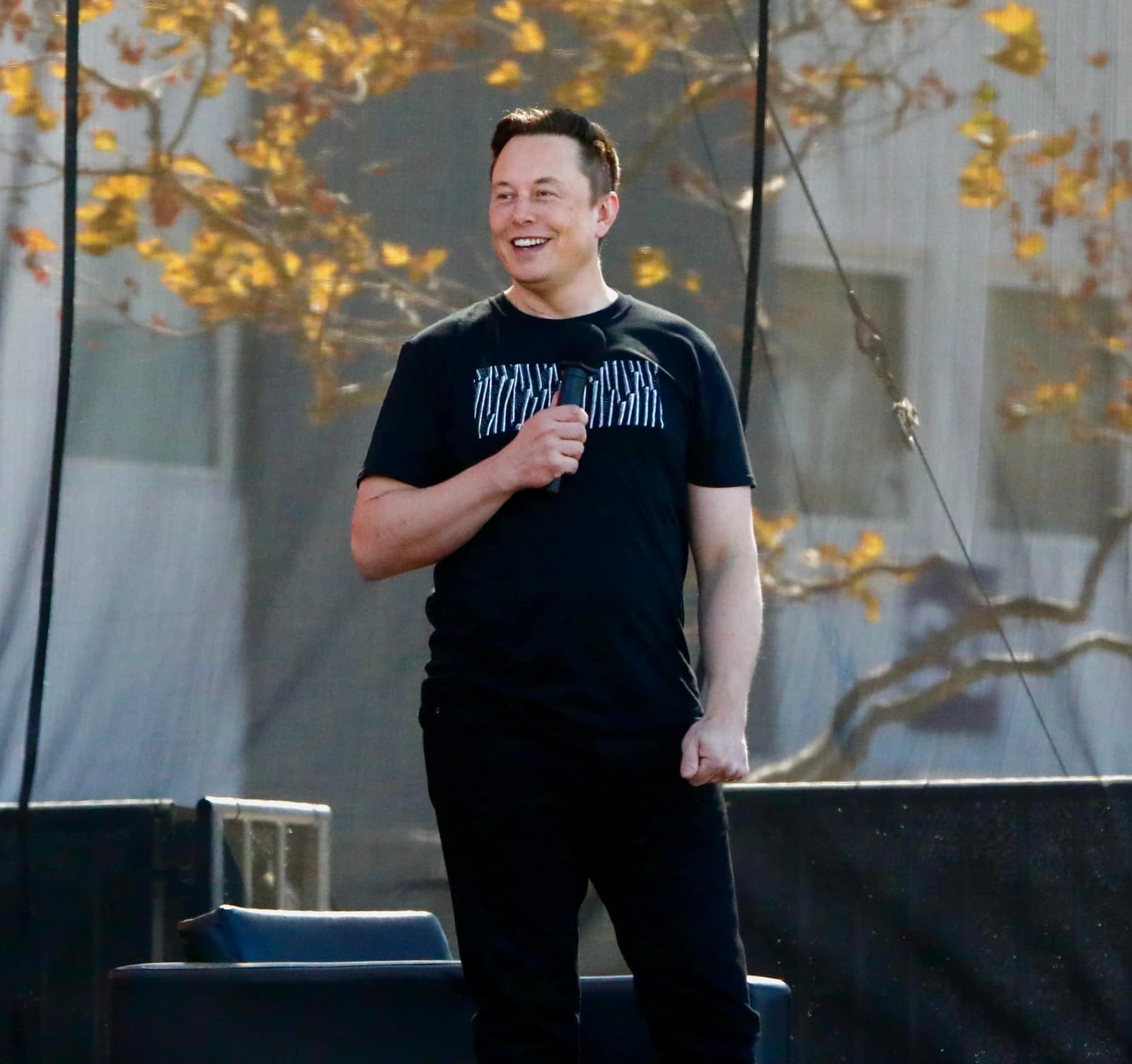 Elon Musk, CEO of Tesla and SpaceX, speaking into a microphone outdoors.