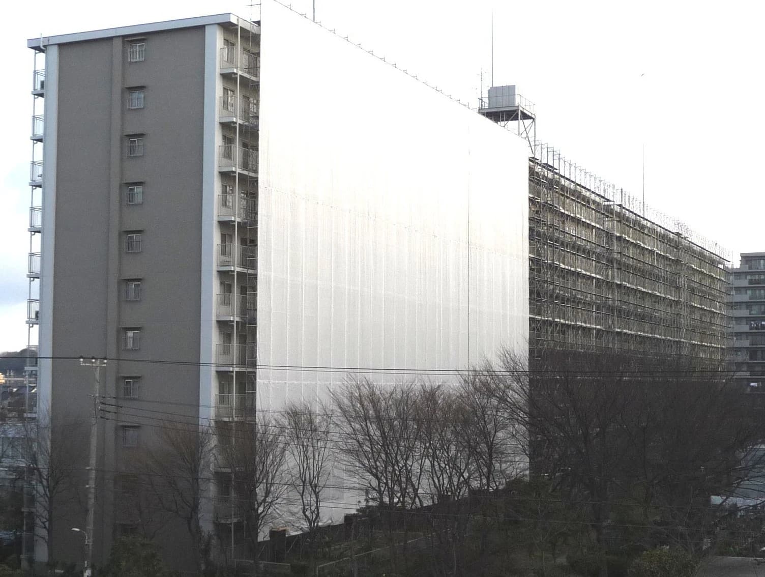 Tall condominium building in Japan with one side covered in white protective sheeting.