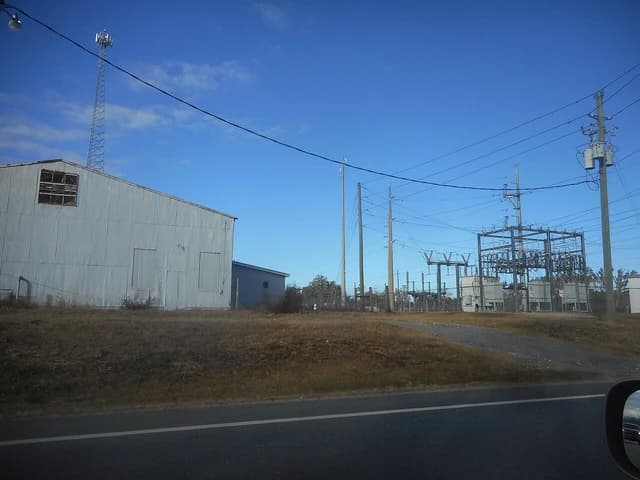Power substation with transformers and electrical infrastructure next to a corrugated metal building.