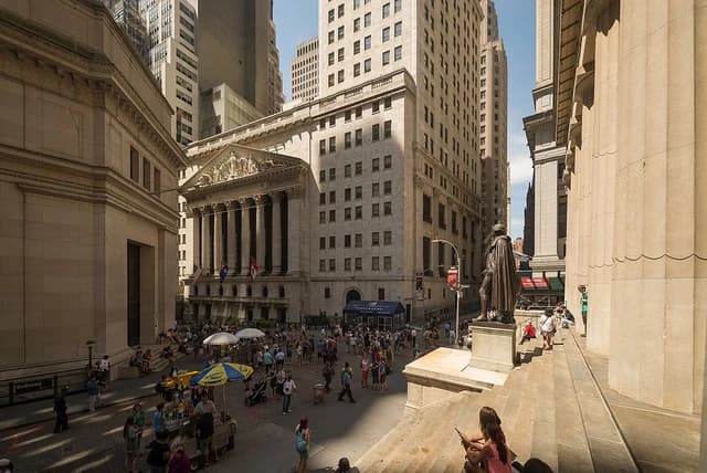 Exterior of the New York Stock Exchange building with crowds on Wall Street.