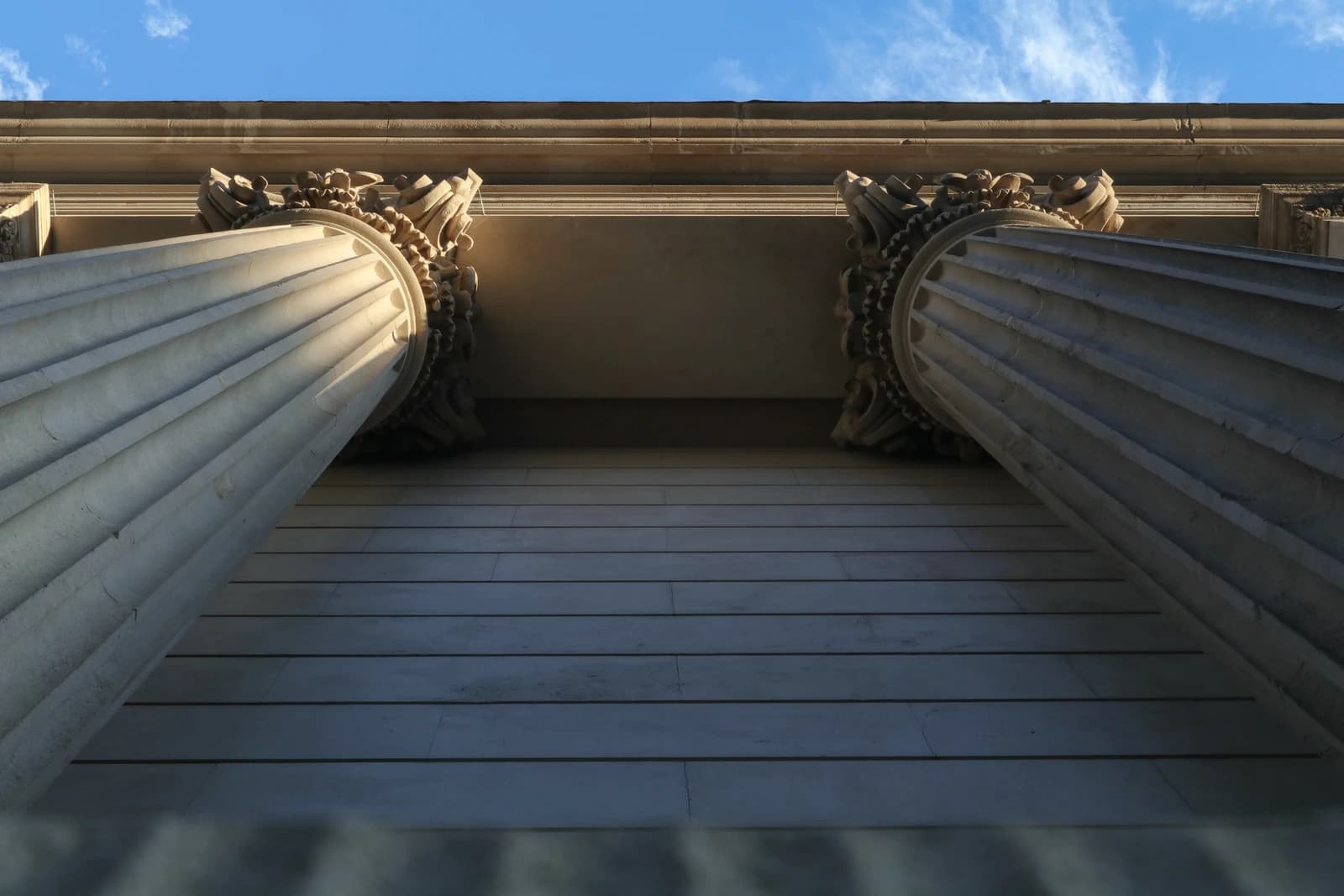Bank of England building's classic architectural columns and entablature viewed from below against blue sky.