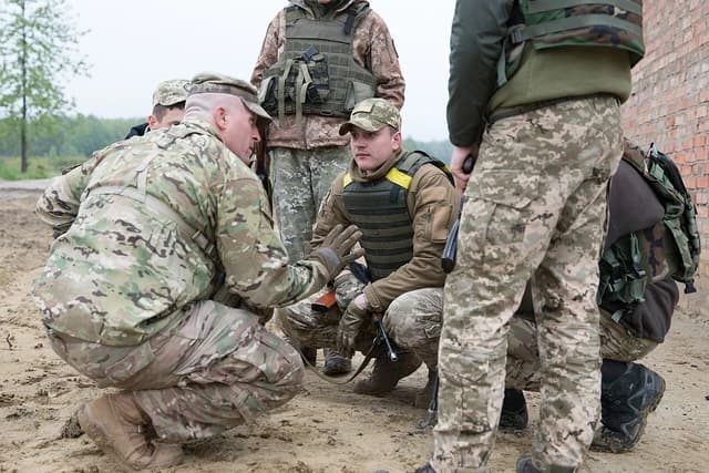Soldiers in camouflage uniforms training in a dirt field in Ukraine.