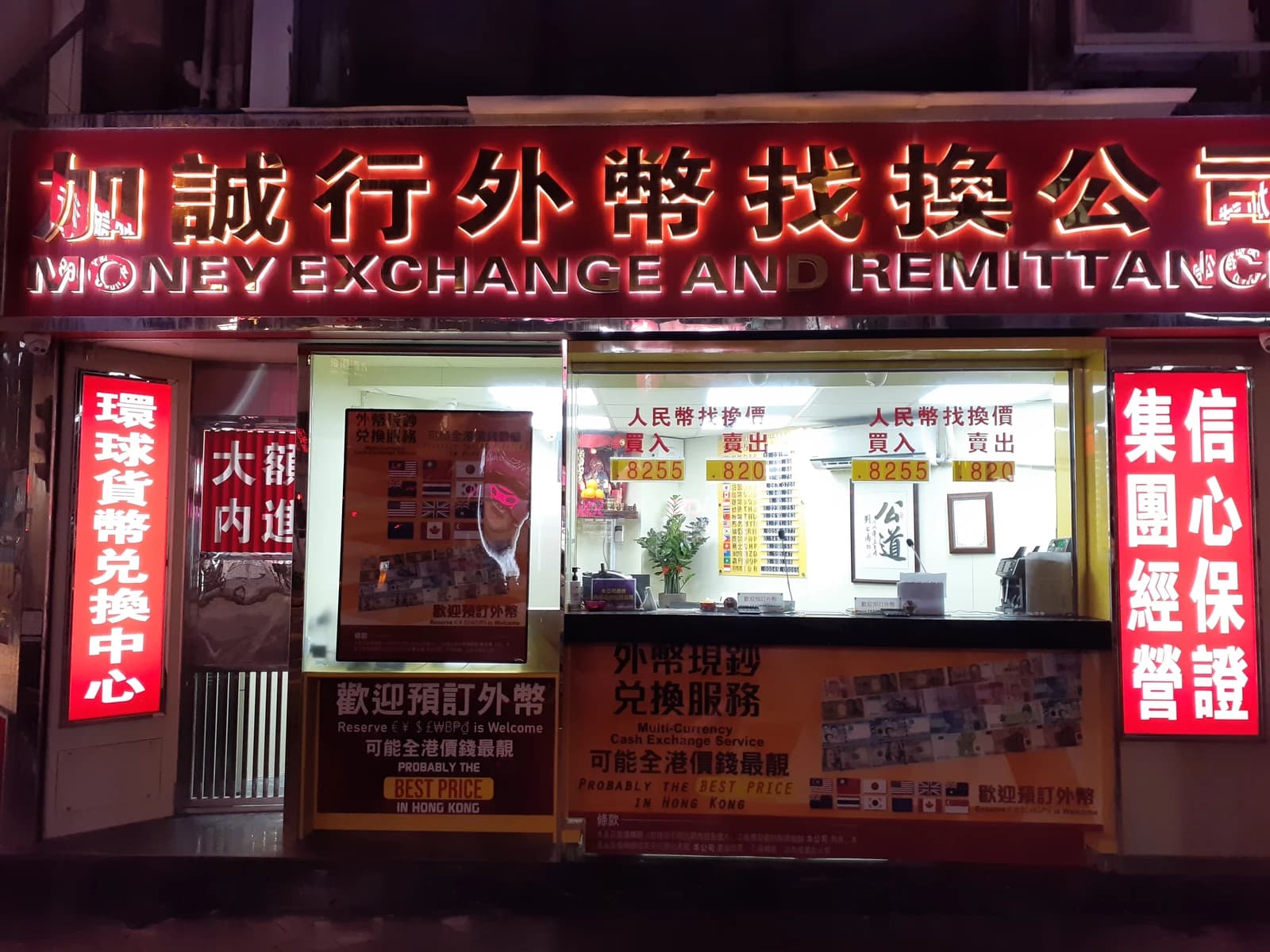 Exterior of a brightly lit 'Money Exchange and Remittance' shop with exchange rates displayed.