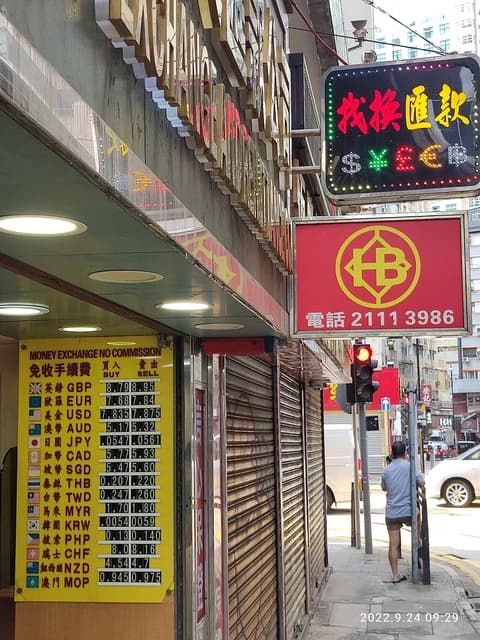 Money exchange rate board displaying various currency exchange rates, including USD, on a street.