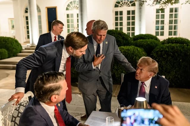 Donald Trump seated at a table with guests at an outdoor dinner event.