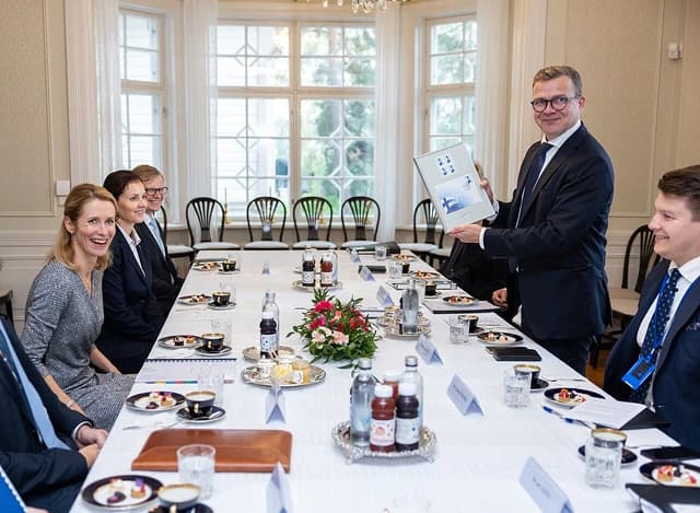 Petteri Orpo, Prime Minister of Finland, holding a framed gift while sitting at a meeting table with Kaja Kallas, Prime Minister of Estonia.