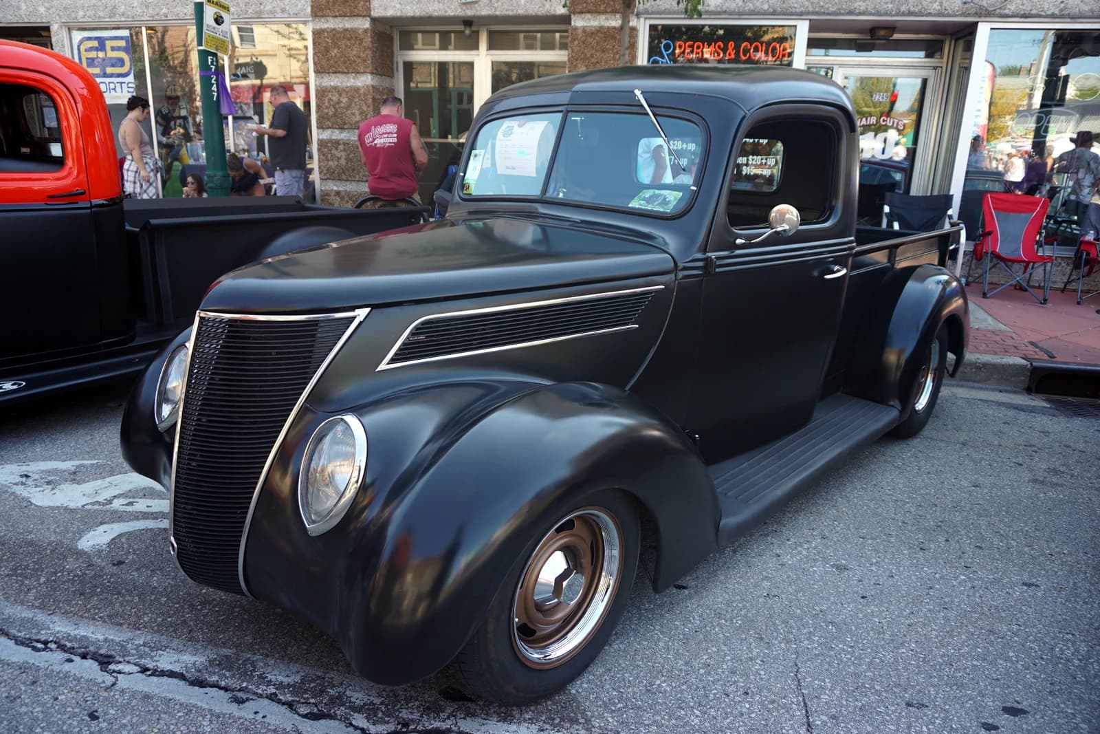 Black 1937 Ford pickup truck parked on street during car show.