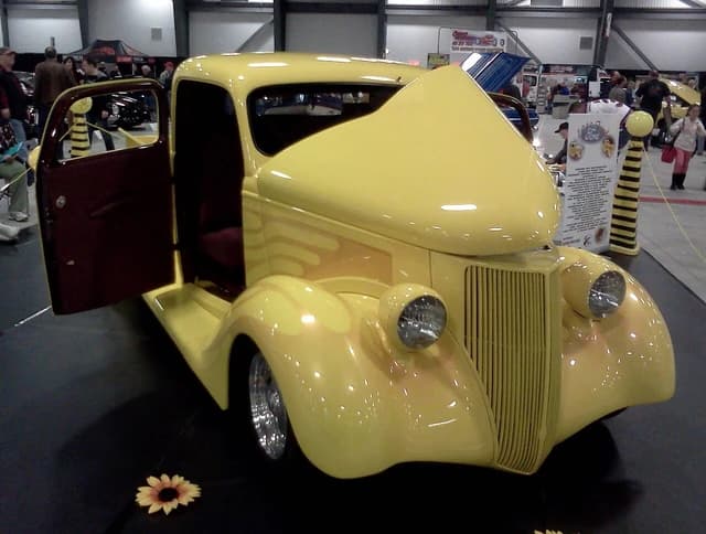 Yellow 1936 Ford Pickup truck with open hood and door at a car show.