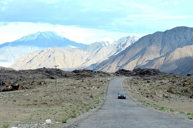 A car drives on the Karakoram Highway through mountains in Pakistan.
