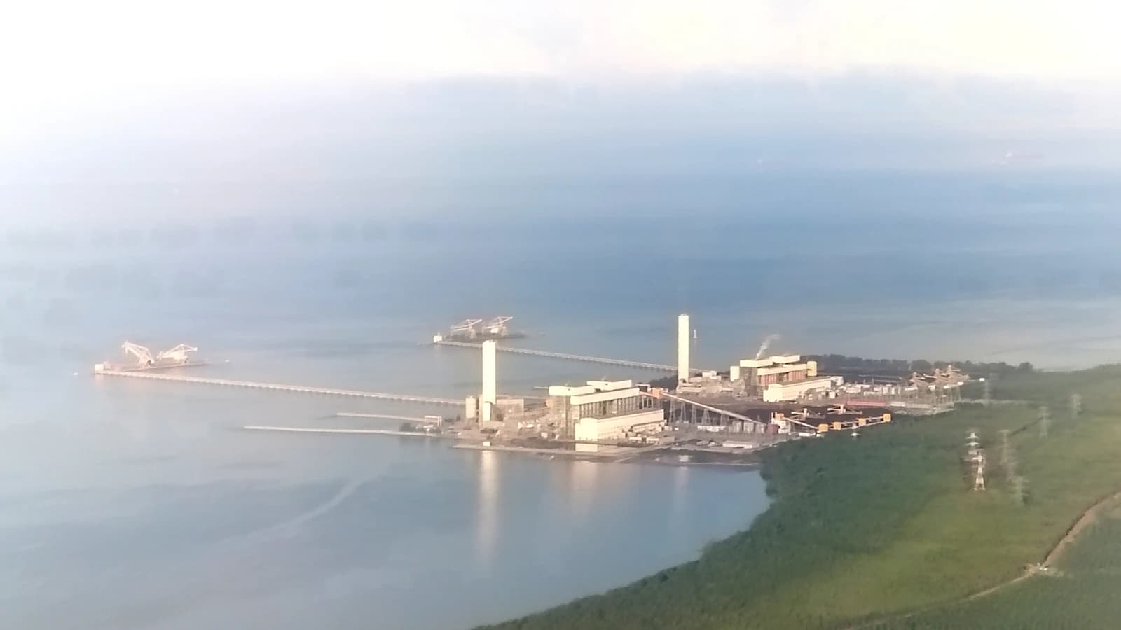 Aerial view of a coal-fired power plant located by the sea with cargo cranes.