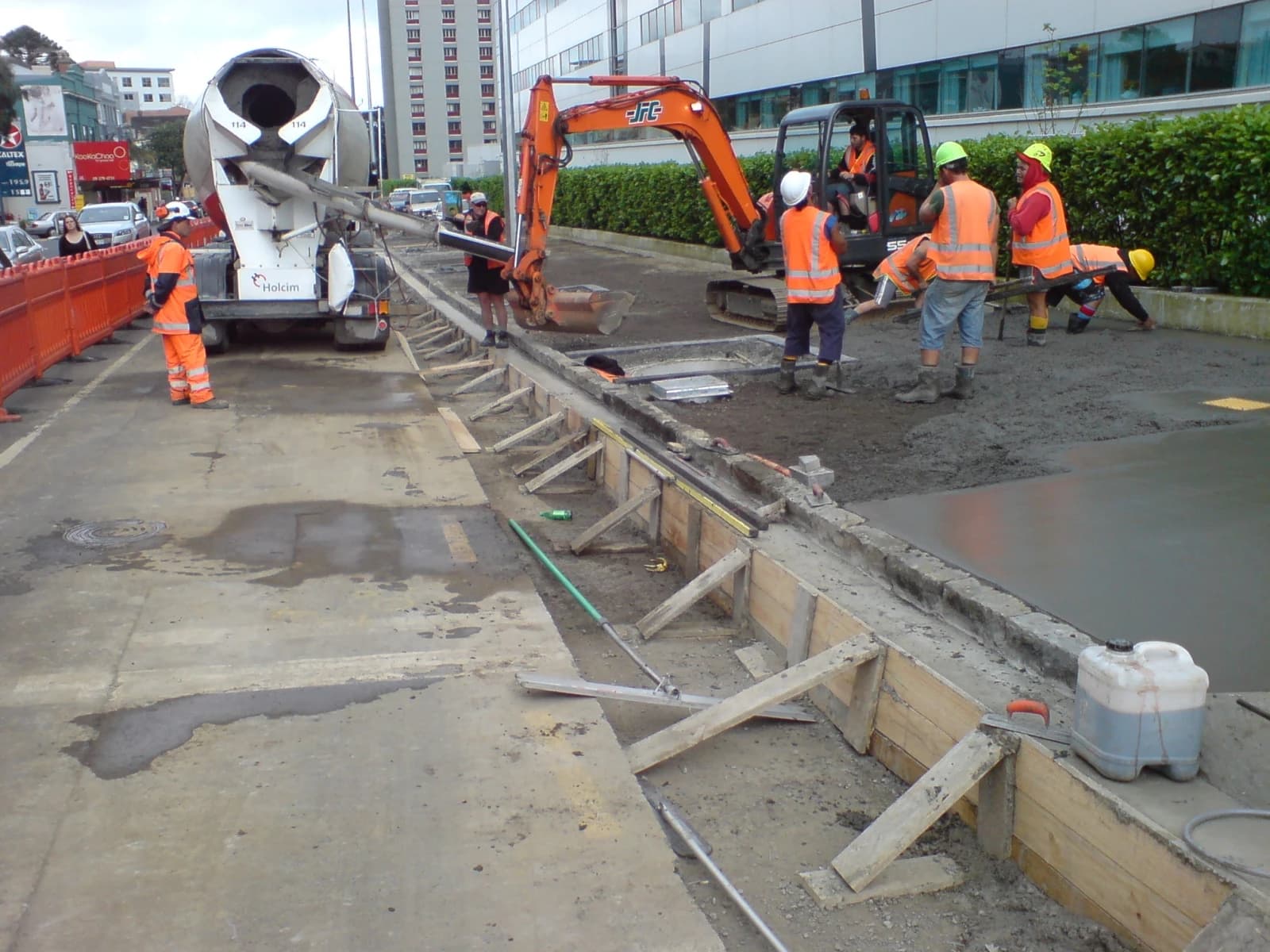 Construction workers pour concrete from a mixer truck for a kerb and channel.