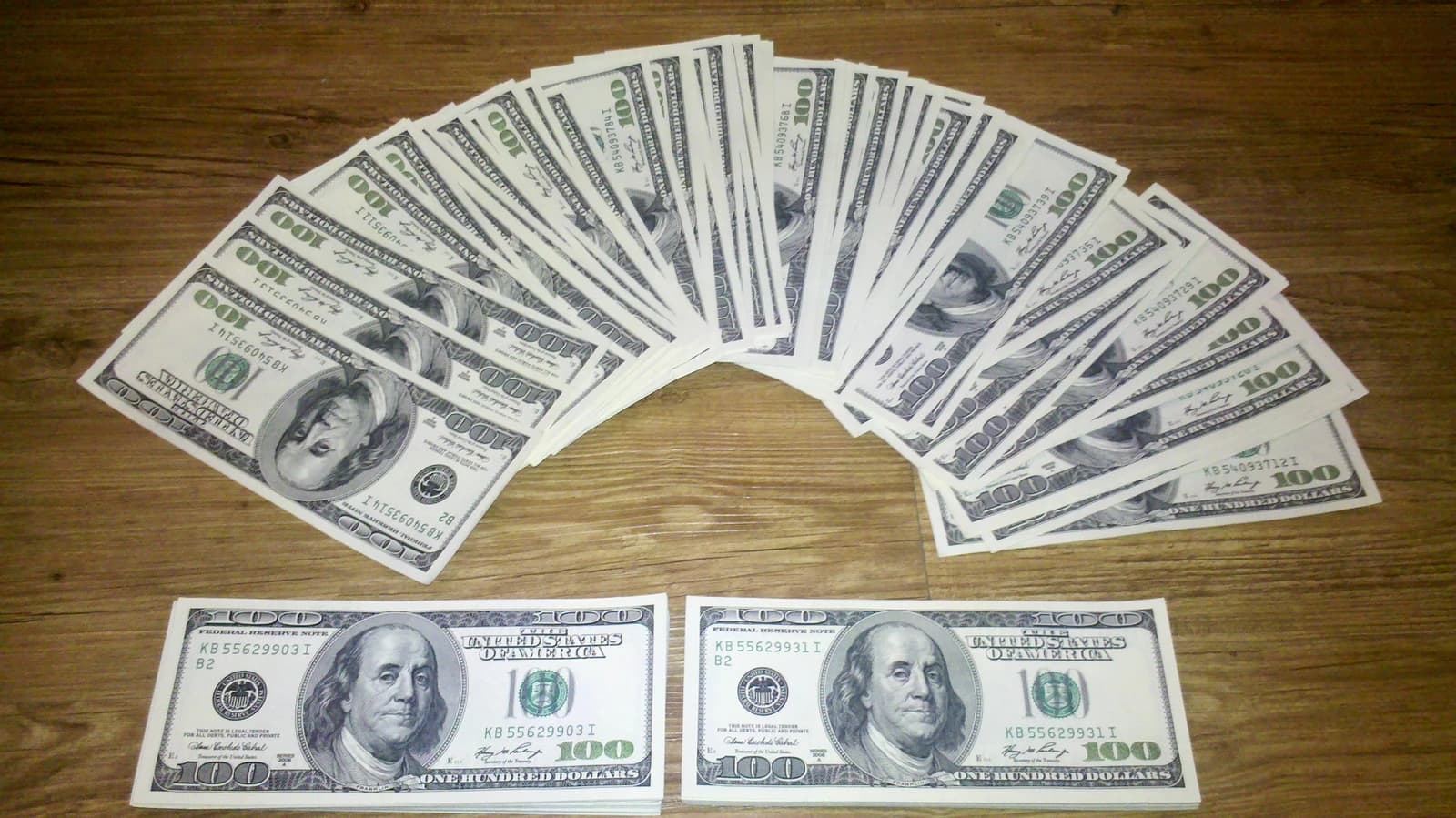 Several hundred US Dollar bills fanned out and stacked on a wooden table.