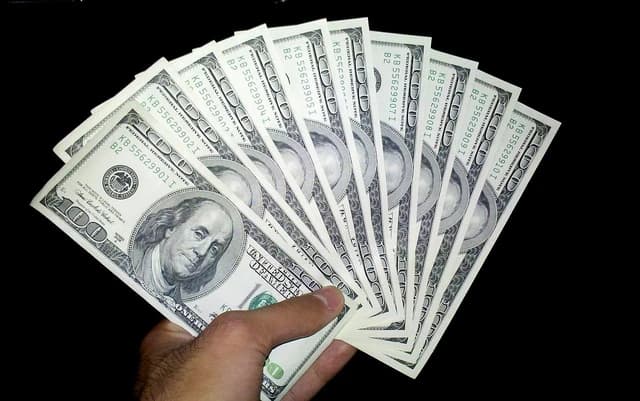 Hand holding a fan of one hundred US dollar banknotes.