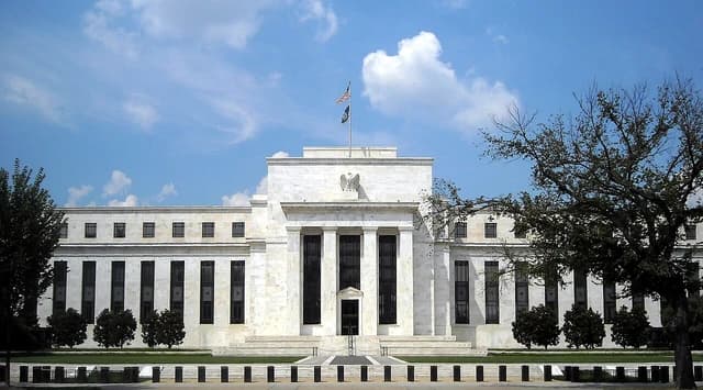 Marriner S. Eccles Federal Reserve Board Building, a white marble structure with columns, under a blue sky.