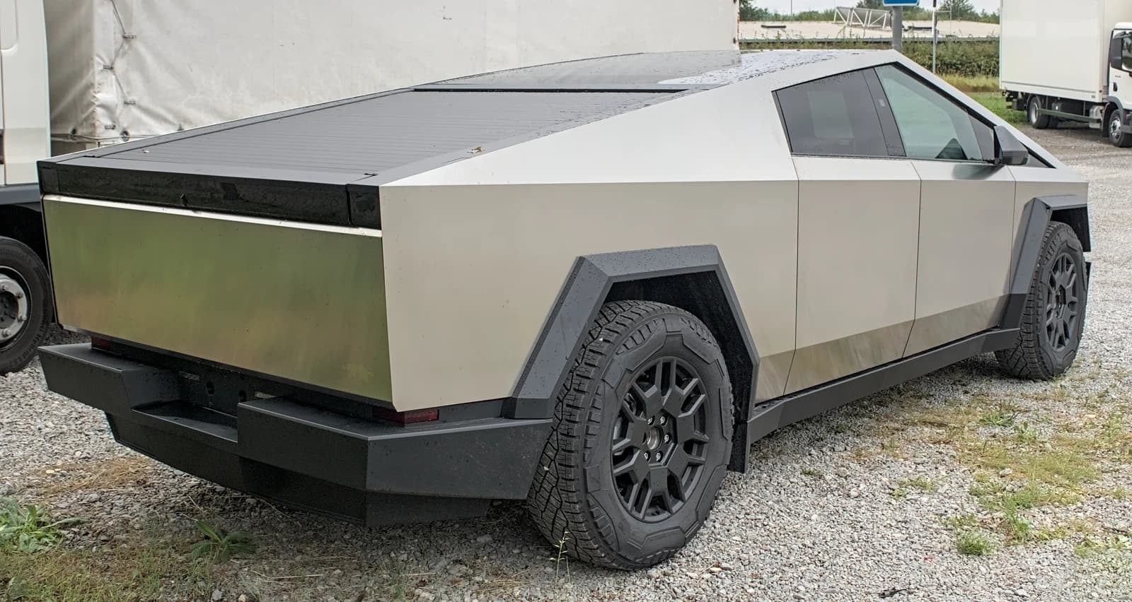 Rear three-quarter view of a Tesla Cybertruck parked on gravel.
