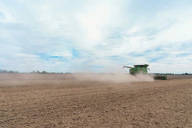 Green combine harvester operating in a dusty field under a cloudy sky.