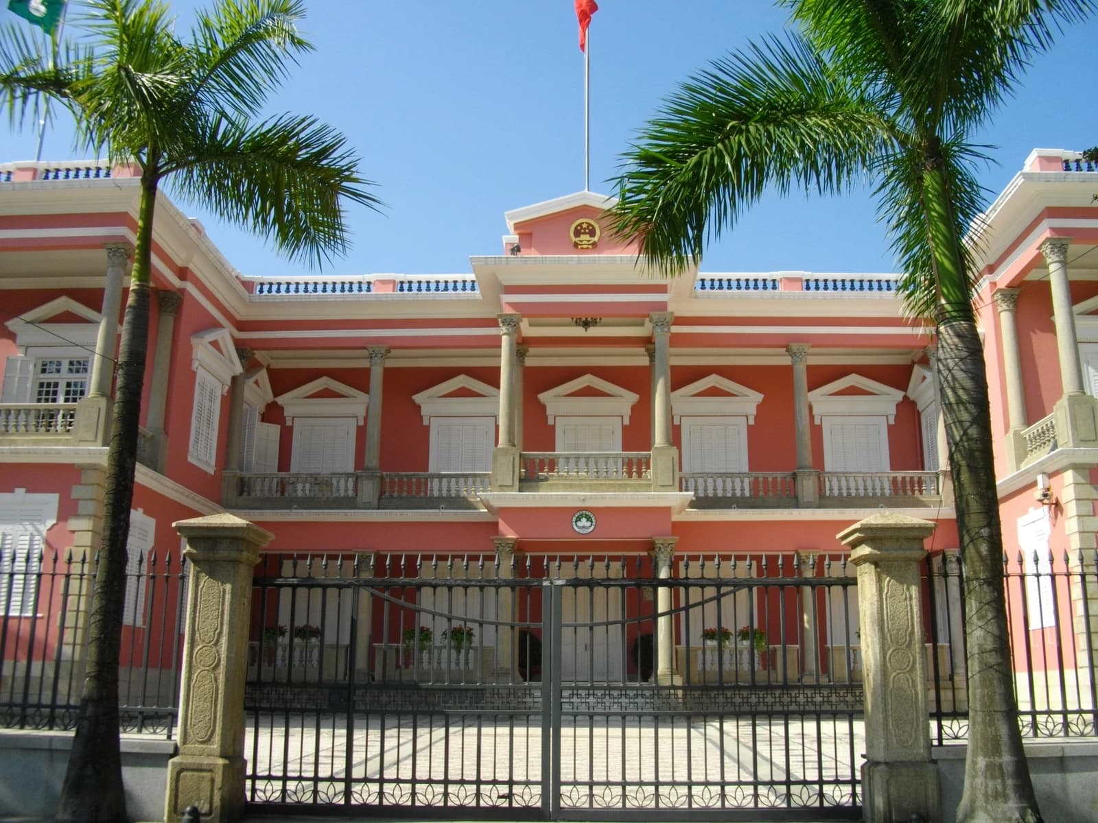 Macau Government Headquarters building with palm trees and a black metal gate in front.