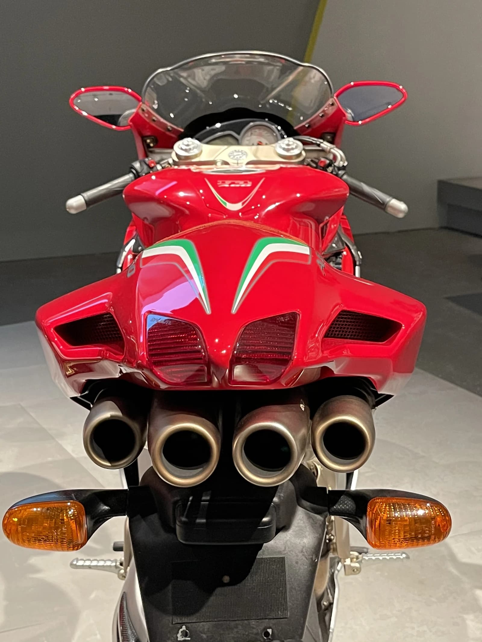 Rear view of a red MV Agusta F4 Ago motorcycle with four exhaust pipes and turn signals.