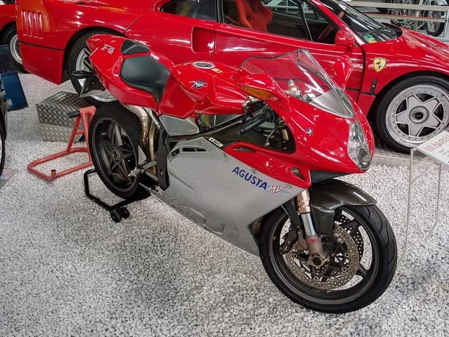 MV Agusta F4 motorcycle parked indoors with a Ferrari car behind it.