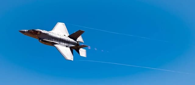 F-35 Lightning II fighter jet flying against a clear blue sky, showing its underside.
