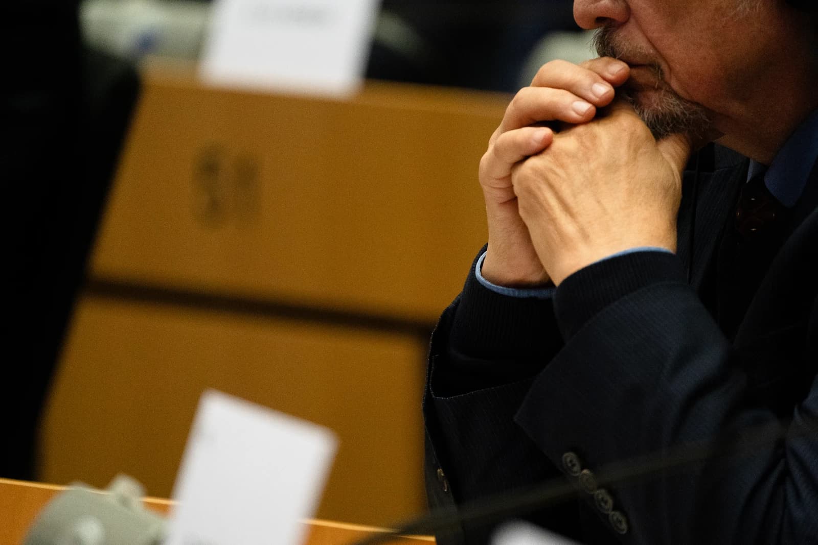 Man with beard, possibly a Commissioner-designate, listens intently during European Parliament hearings.