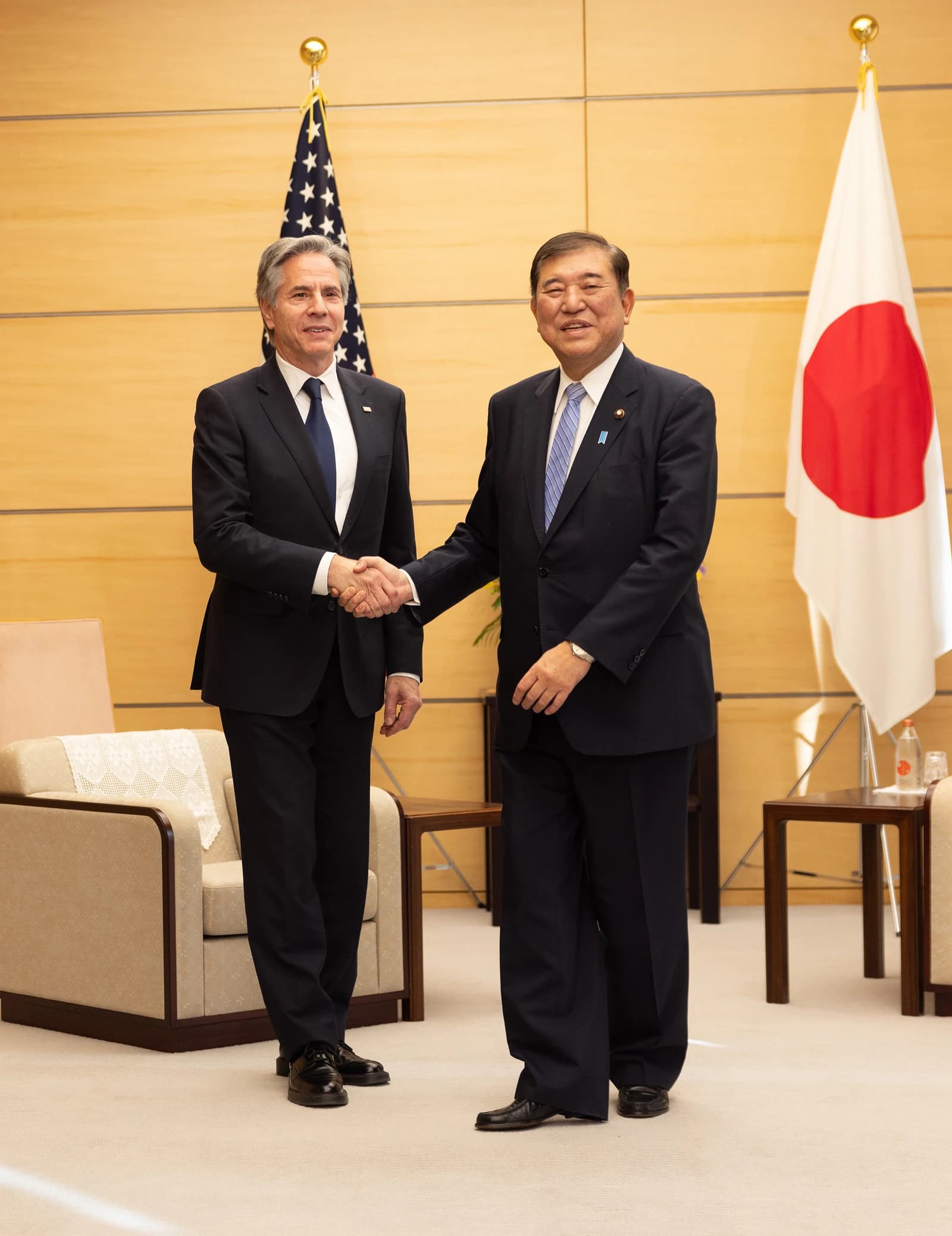 Secretary Blinken and Japanese Prime Minister shaking hands in a room with flags.