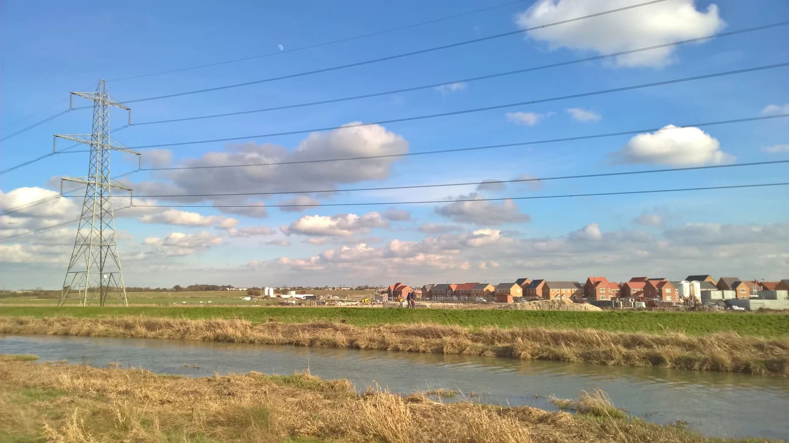 New houses under construction with an electricity pylon and a river in the foreground.
