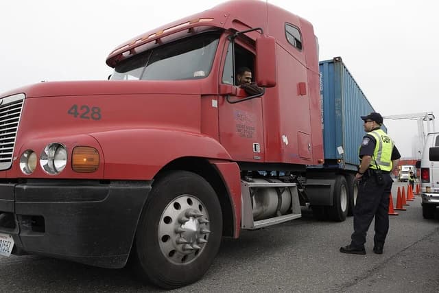U.S. Customs and Border Protection officer inspects a commercial truck carrying a shipping container.