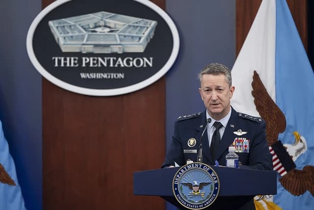 General Dan Caine speaking at a podium with a Pentagon logo in the background.