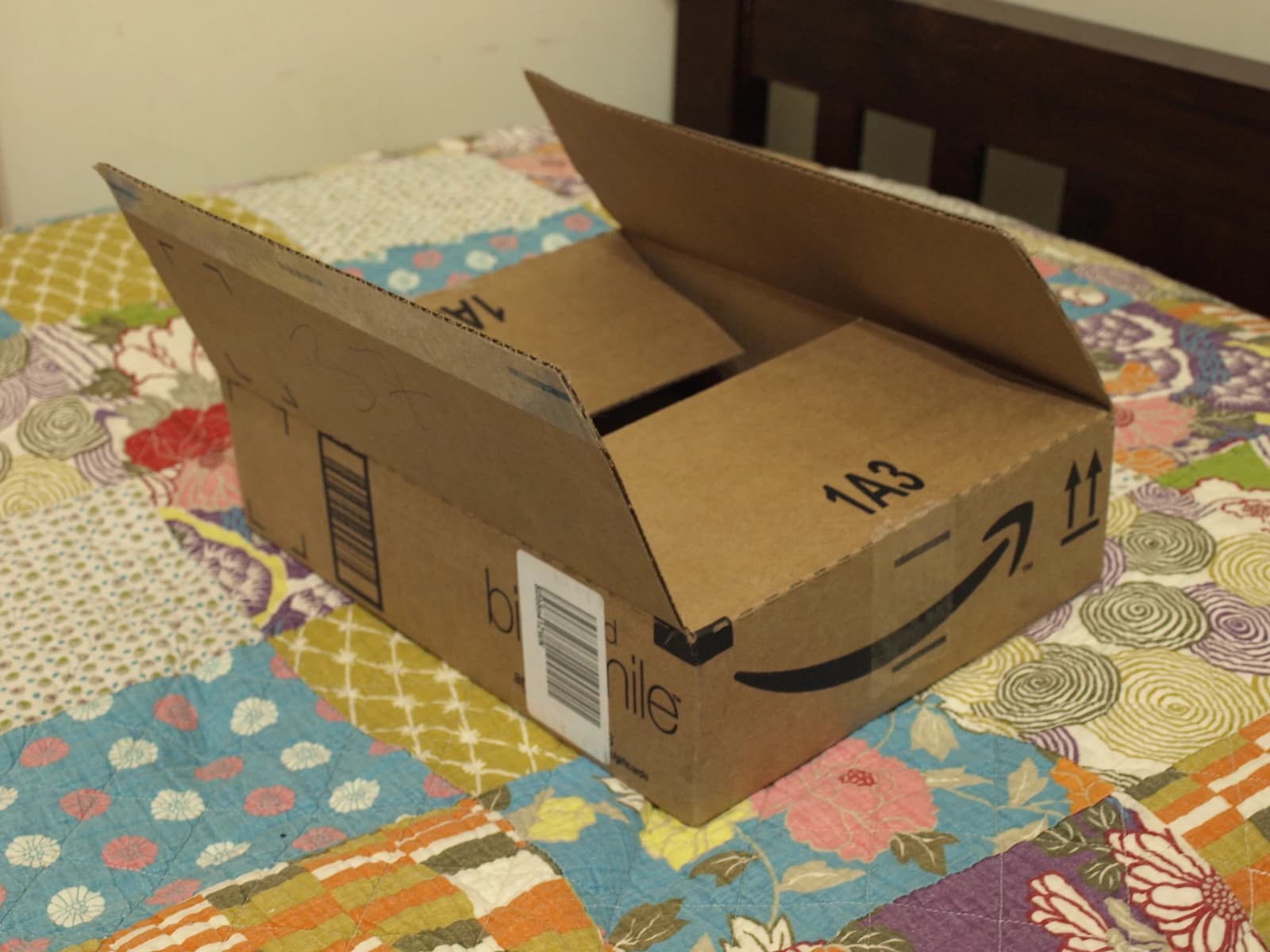 An empty, open Amazon delivery box rests on a colorful, patterned quilt.