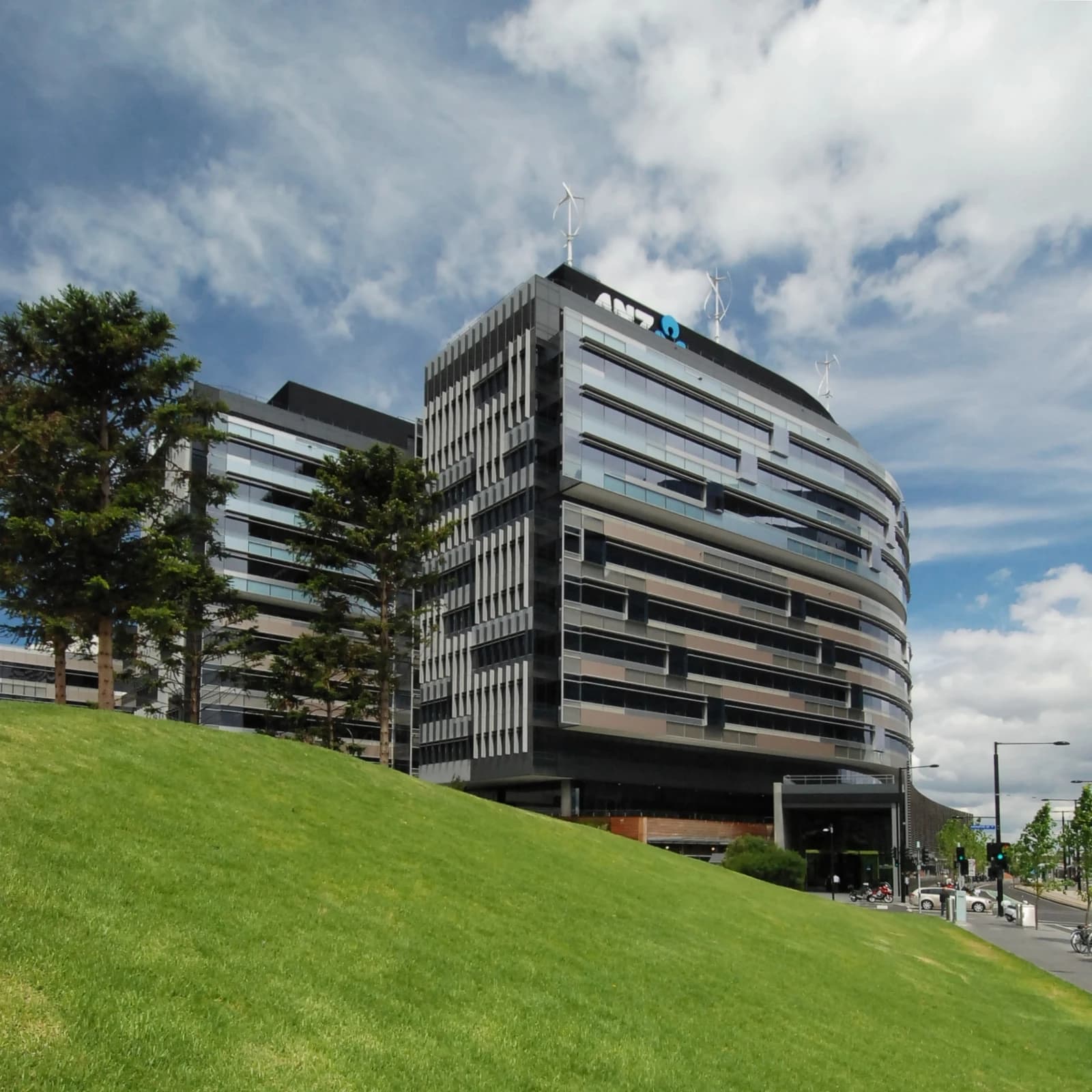 ANZ building in Docklands, Melbourne, with a grassy hill and trees in the foreground.