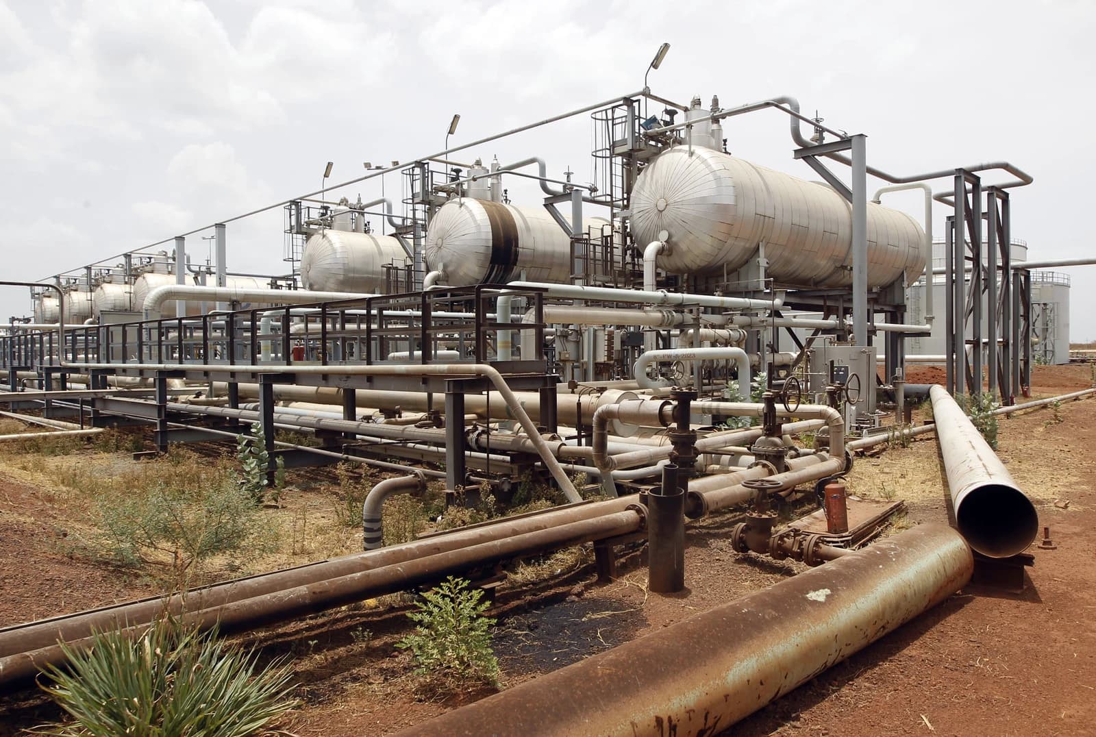 Oil processing facility with large tanks and interconnected pipes under a cloudy sky.