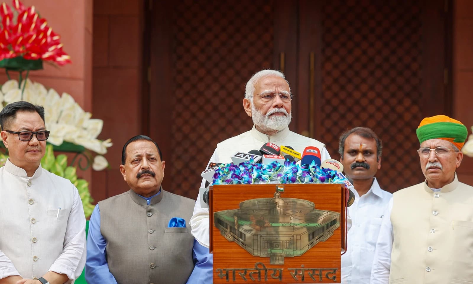 Narendra Modi, Prime Minister of India, speaking at a podium with several men standing nearby.