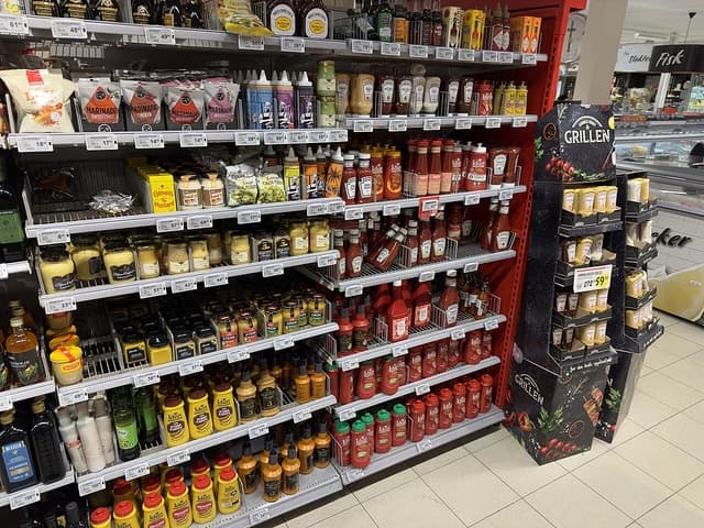 Supermarket aisle with shelves of various bottled sauces, mustards, ketchups, and marinades.