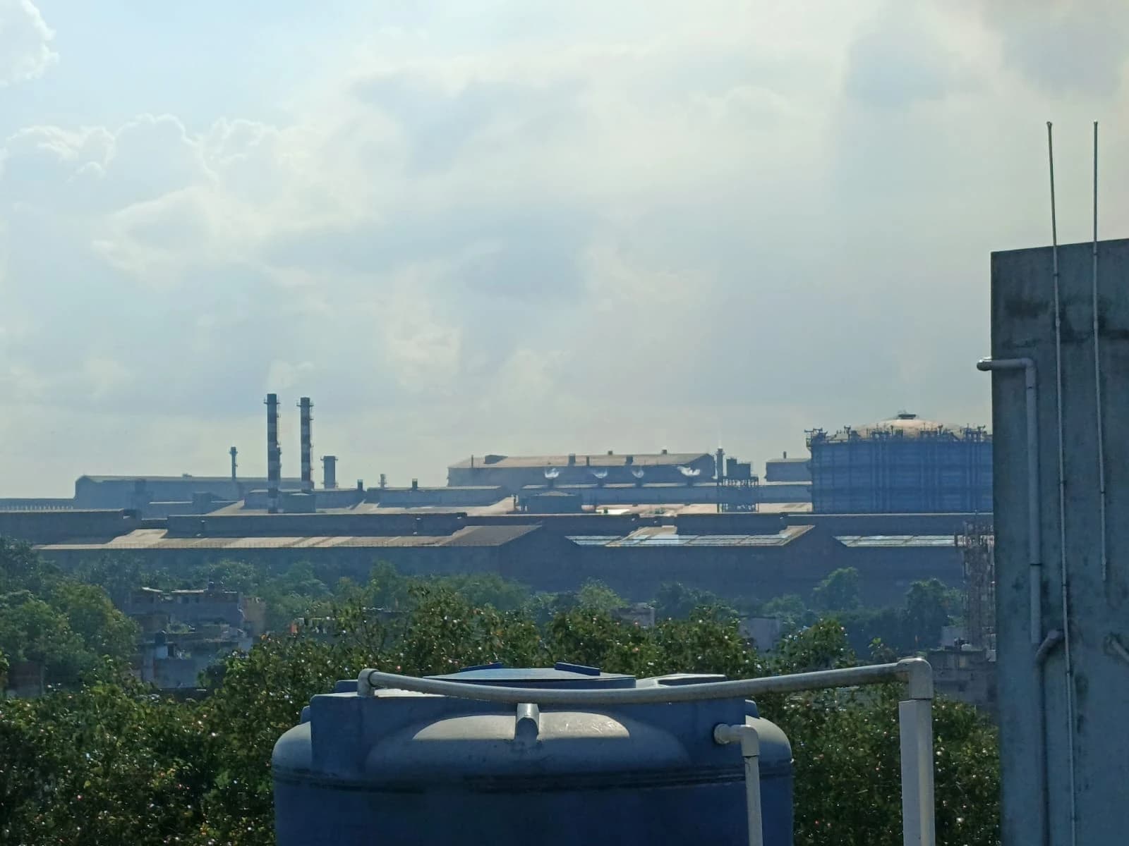 Tata Steel factory buildings with smokestacks under a bright sky.
