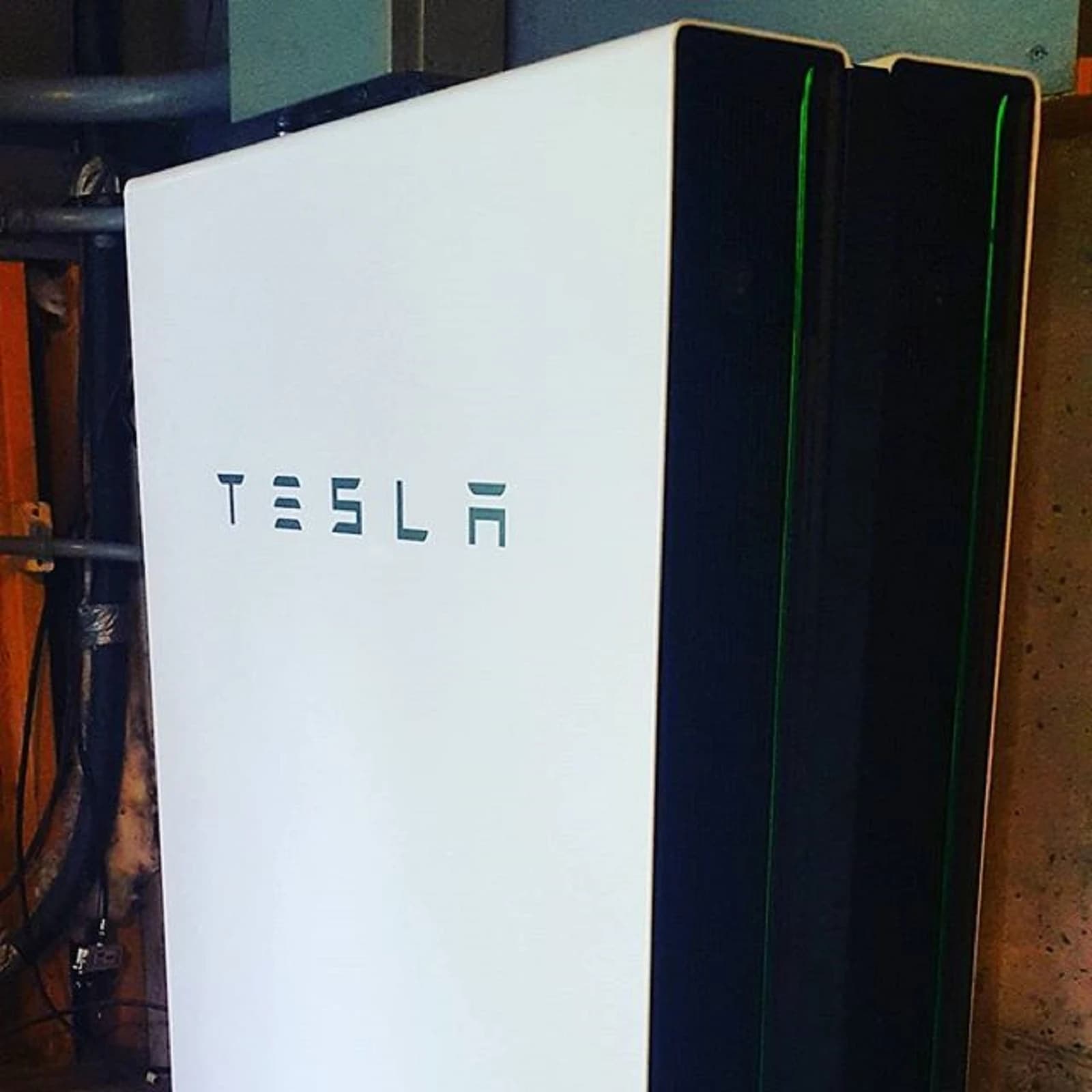 A white Tesla Powerwall home energy storage battery with the Tesla logo.