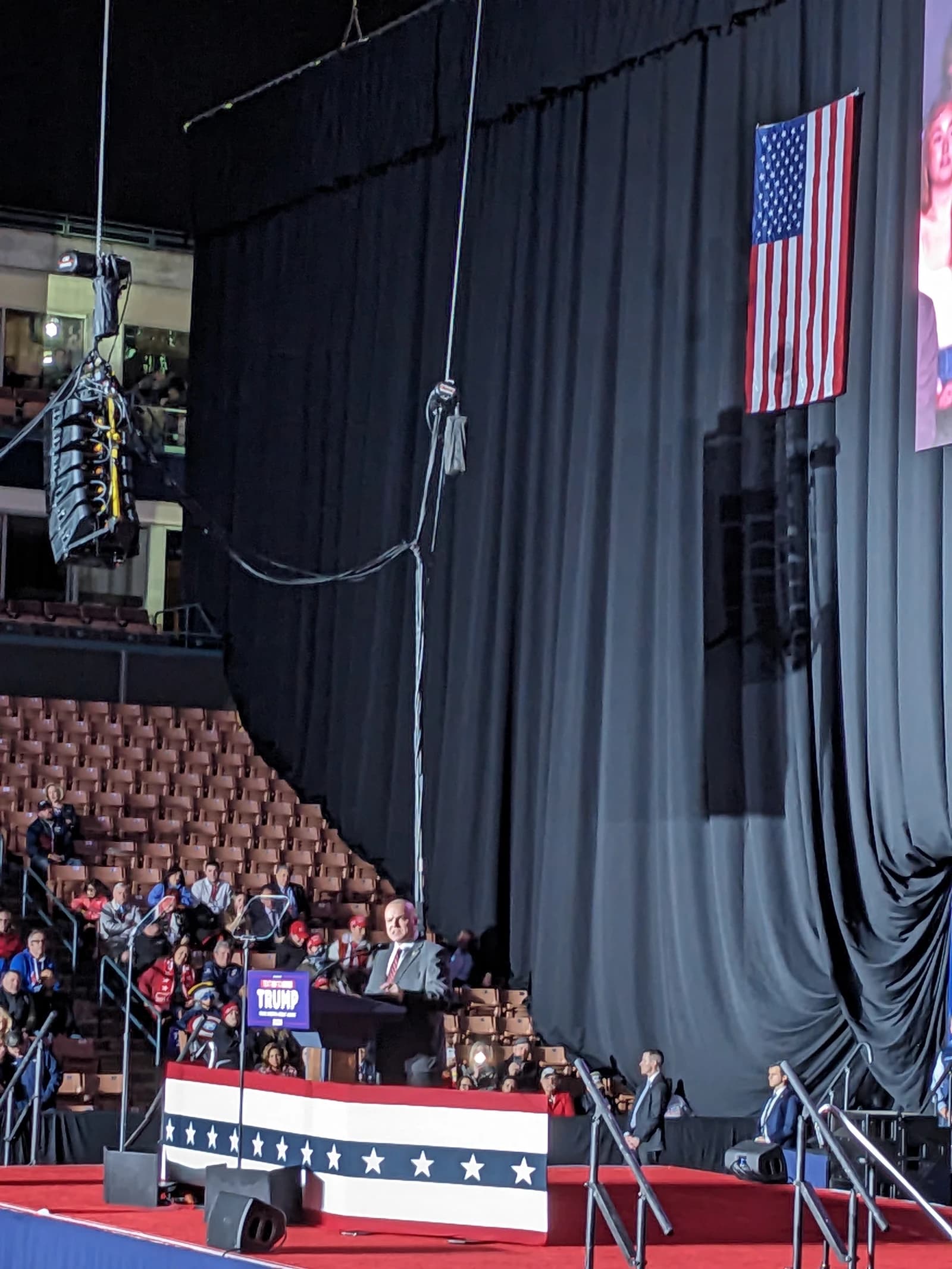 Donald Trump speaking at a podium on a stage in front of a crowd at a rally.