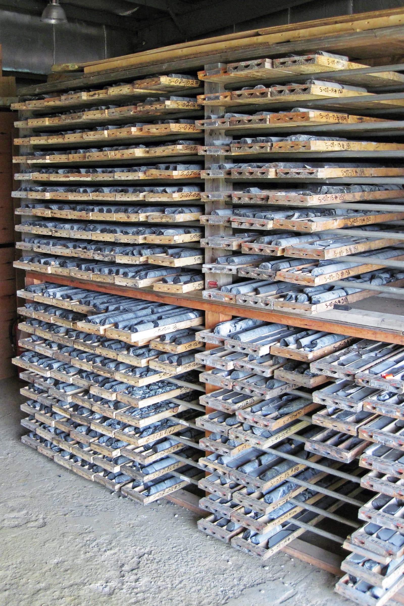 Rows of wooden shelves holding numerous cylindrical rock samples from geological exploration.
