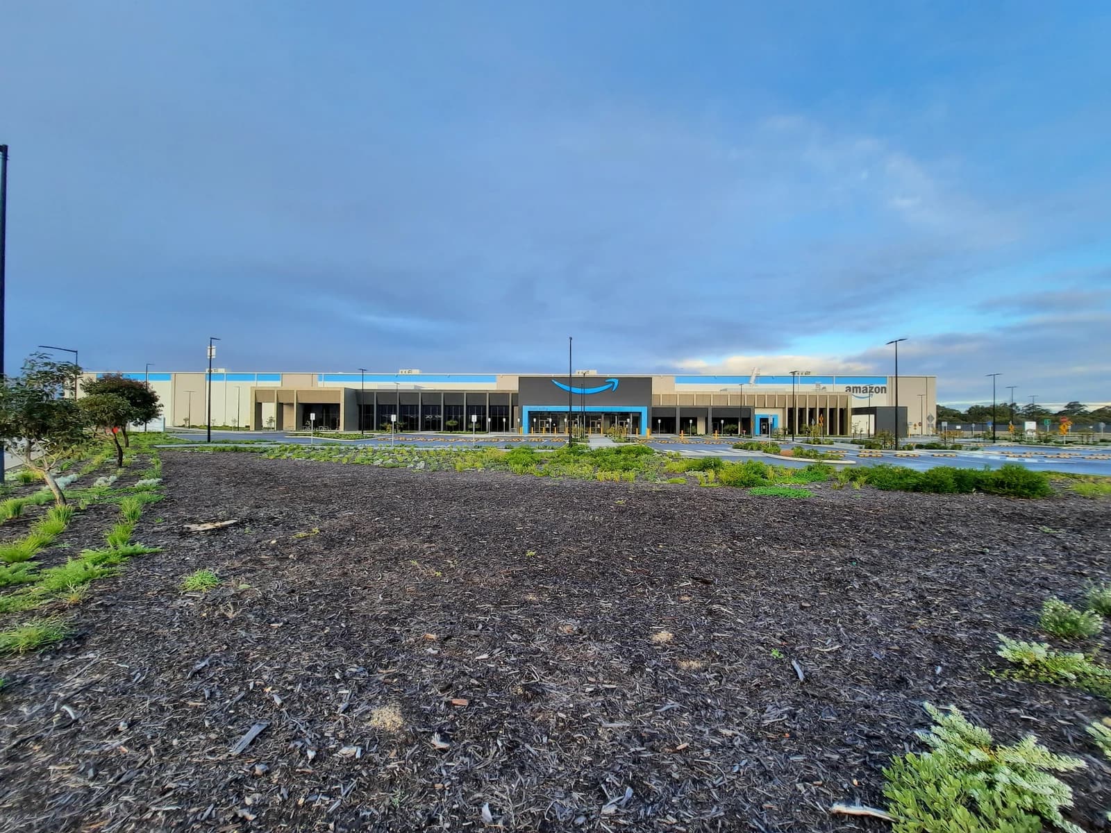 An Amazon distribution center building with its logo visible, under a cloudy sky.
